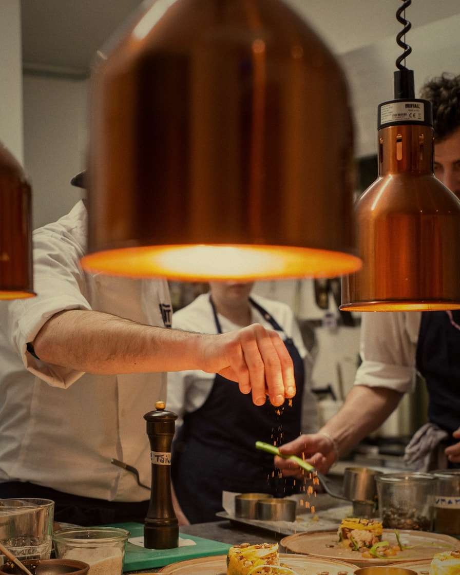 Nella cucina di un ristorante, sotto le lampade di rame, gli chef rifiniscono i piatti prima del servizio