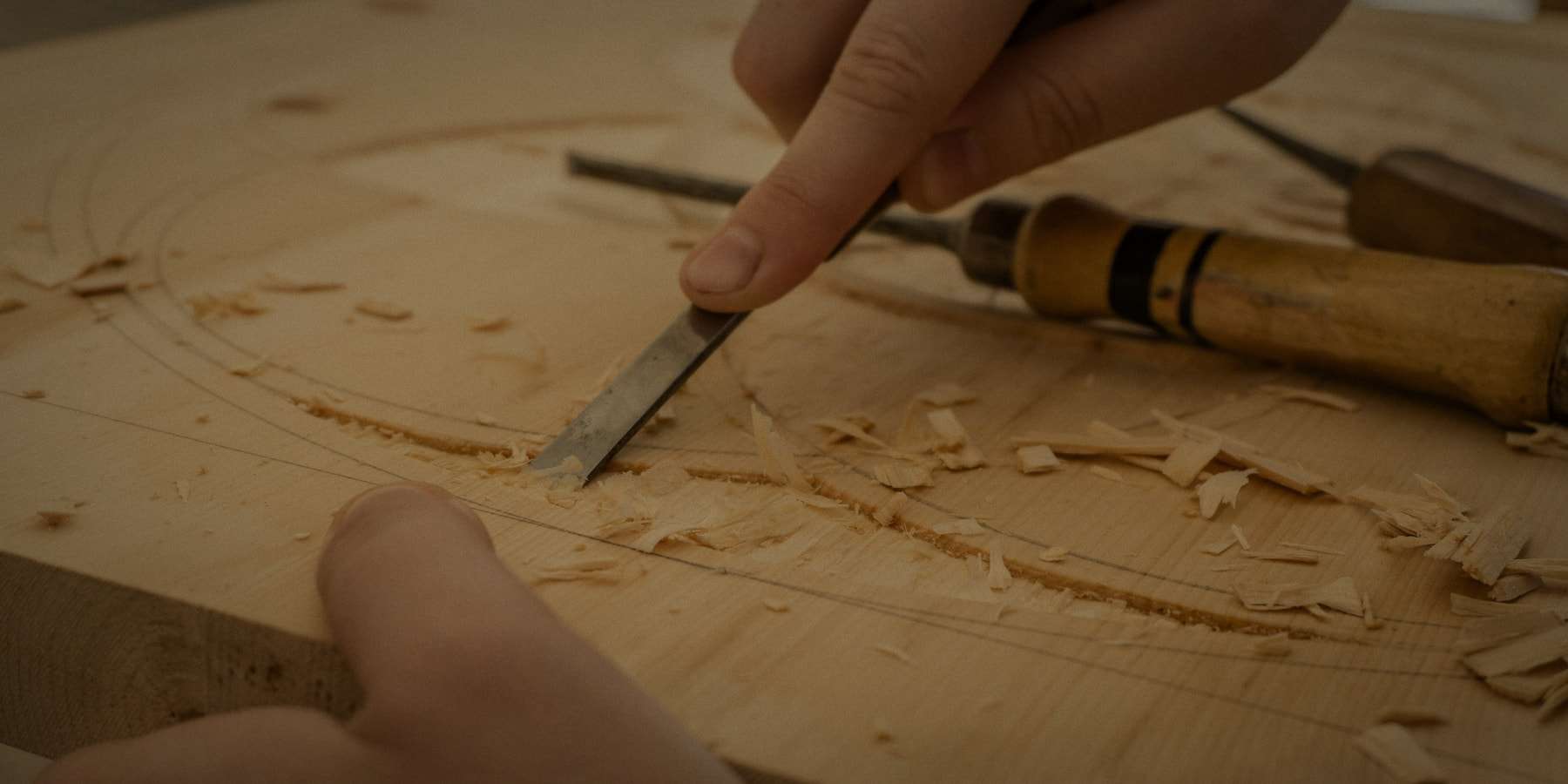 Le mani di un artigiano incidono il legno con lo scalpello, tra i trucioli